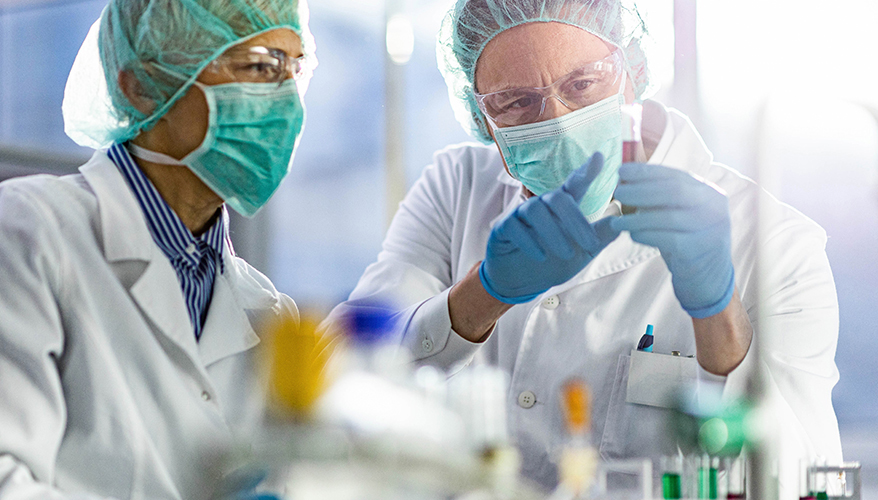 Researchers wearing personal protective equipment look at a vial